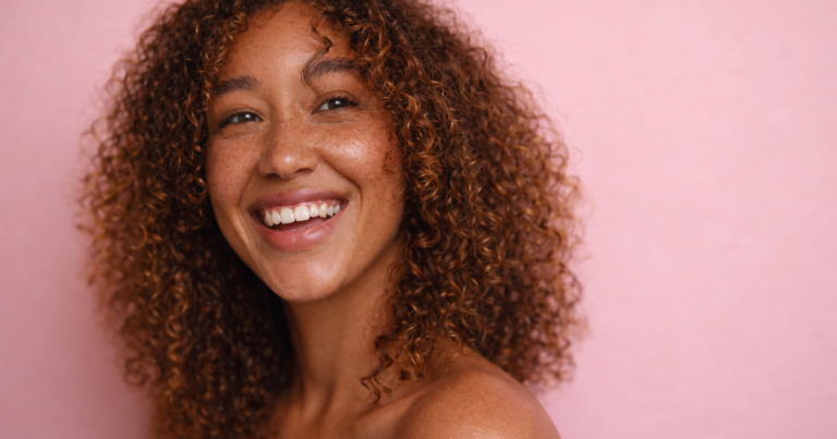 Smiling woman with natural glowing skin against a soft pink background