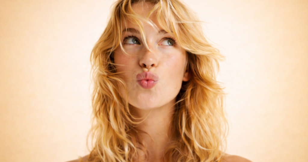 Woman with radiant skin and wavy hair looking to the side on a soft light yellow background.