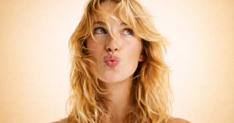 Woman with radiant skin and wavy hair looking to the side on a soft light yellow background.
