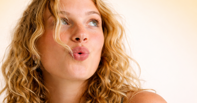 Woman with natural freckled skin on a soft yellow background looking to the side.