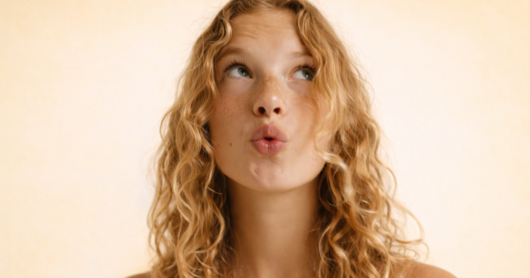 Woman with natural freckled skin on a soft yellow background looking to the side.