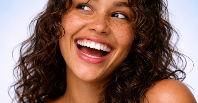 Woman with curly hair and natural skin on a soft blue background looking to the side and laughing.