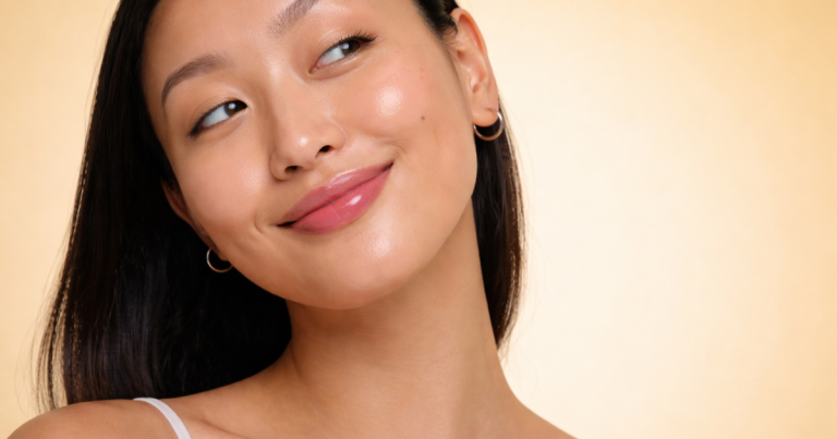Woman with healthy, radiant skin and minimal makeup smiling softly, representing a natural skincare look on a warm yellow background.