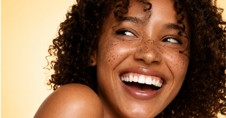 Beauty portrait of a woman with natural freckles and curly hair with a soft light yellow gradient background.